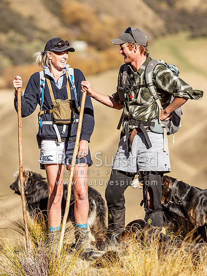 Georgina and James Murray, managers of The Branches Station, with dogs during the autumn muster. Sixteen Mile Hut in the upper Shotover River valley behind, Branches Station, Shotover Valley, Queenstown Lakes District, Otago Region, New Zealand (NZ)