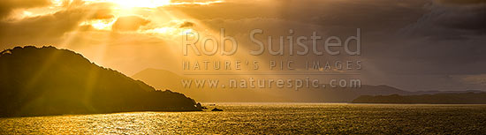 Sunlit rays over Paterson Inlet Whaka a Te Wera. Evening crepusular rays and glowing skies lighting Ulva Island at left. Rakiura panorama, Paterson Inlet, Stewart Island District, Southland Region, New Zealand (NZ)