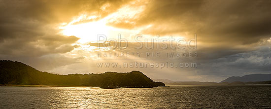 Sunlit rays over Paterson Inlet Whaka a Te Wera. Evening crepusular rays and glowing skies lighting Ulva Island at left. Rakiura panorama, Paterson Inlet, Stewart Island District, Southland Region, New Zealand (NZ)