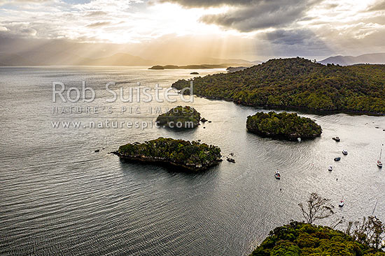 Faith, Hope and Charity Group of islands in Paterson Inlet Whaka a Te Wera. Glowing evening skies of Rakiura beyond. Aerial view, Paterson Inlet, Stewart Island District, Southland Region, New Zealand (NZ)