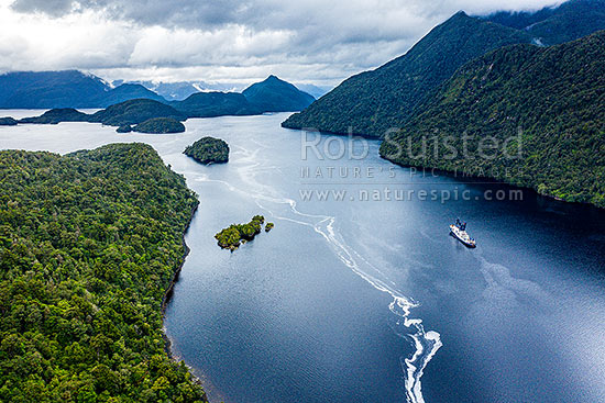 Cascade Cove, off Cook Channel in Dusky Sound. Ship anchored in the protected anchorage. Heron Island, Curlew Island and Long Island behind. Aerial view, Dusky Sound, Fiordland National Park, Southland District, Southland Region, New Zealand (NZ)