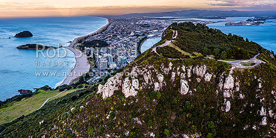 Mt Maunganui summit Mauao at the Tauranga Harbour Entrance. 231m high lava dome. Mt Maunganui Beach left, Tauranga Harbour right. Aerial panorama at dusk, Mount Maunganui, Tauranga District, Bay of Plenty Region, New Zealand (NZ)