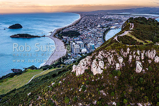 Mt Maunganui summit Mauao at the Tauranga Harbour Entrance. 231m high lava dome. Mt Maunganui Beach left, Tauranga Harbour right. Aerial view at dusk, Mount Maunganui, Tauranga District, Bay of Plenty Region, New Zealand (NZ)