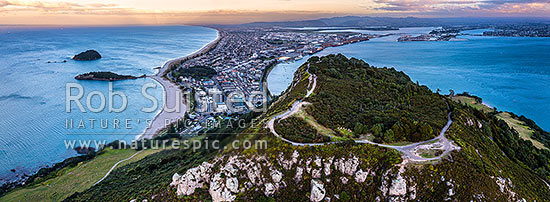 Mt Maunganui summit Mauao at the Tauranga Harbour Entrance. 231m high lava dome. Mt Maunganui Beach left, Tauranga Harbour right. Aerial panorama at dusk, Mount Maunganui, Tauranga District, Bay of Plenty Region, New Zealand (NZ)