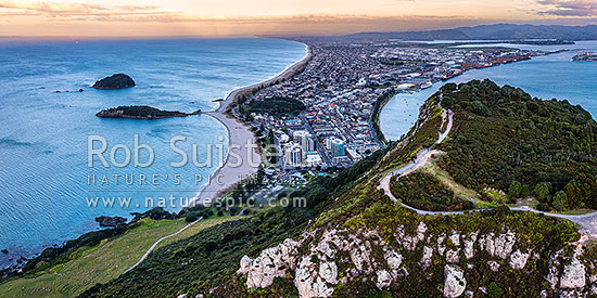 Mt Maunganui summit Mauao at the Tauranga Harbour Entrance. 231m high lava dome. Mt Maunganui Beach left, Tauranga Harbour right. Aerial panorama at dusk, Mount Maunganui, Tauranga District, Bay of Plenty Region, New Zealand (NZ)