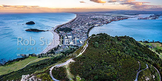 Mt Maunganui summit Mauao at the Tauranga Harbour Entrance. 231m high lava dome. Mt Maunganui Beach left, Tauranga Harbour right. Aerial view at dusk, Mount Maunganui, Tauranga District, Bay of Plenty Region, New Zealand (NZ)