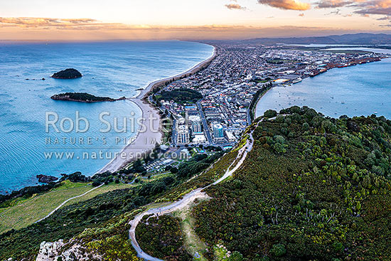 Mt Maunganui summit Mauao at the Tauranga Harbour Entrance. 231m high lava dome. Mt Maunganui Beach left, Tauranga Harbour right. Aerial view at dusk, Mount Maunganui, Tauranga District, Bay of Plenty Region, New Zealand (NZ)