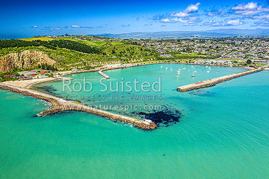 Oamaru harbour breakwater and Holmes Wharf (right) enclosing Friendly Bay, with Oamaru Blue Penguin Colony and Cape Wanbrow beyond at left. Aerial view, Oamaru, Waitaki District, Canterbury Region, New Zealand (NZ)