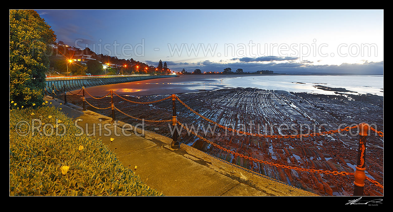 Image of Tahunanui Beach evening sunset panorama with dramatic geologial rock patterns in foreground, and Rocks Road, Moana, left, Nelson, Nelson City District, Nelson Region, New Zealand (NZ) stock photo image